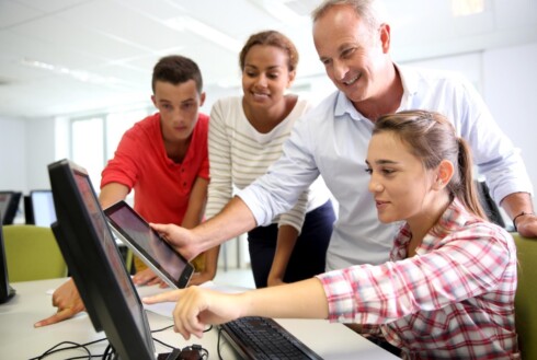 Teacher views screens in tech lab with students